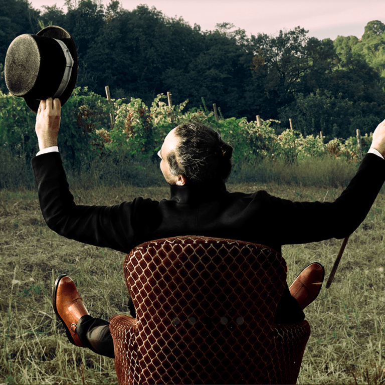 Tommaso Gallina, ASOTOM winemaker, in a chair in the middle of a field with arms and legs akimbo.